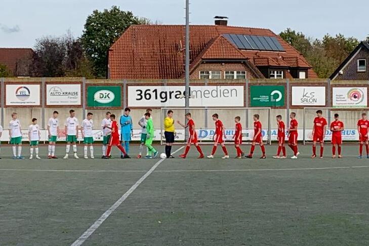 Zwei Fu&szlig;ballmannschaften in wei&szlig;en und roten Trikots stehen sich auf einem Platz gegen&uuml;ber, bereit zum Anpfiff.