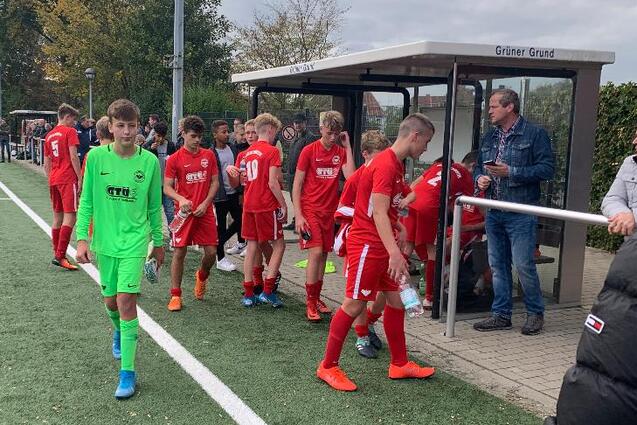 Gruppe junger Fu&szlig;ballspieler in roten Trikots verl&auml;sst das Spielfeld, w&auml;hrend ein Torwart in Gr&uuml;n zum Platz geht.