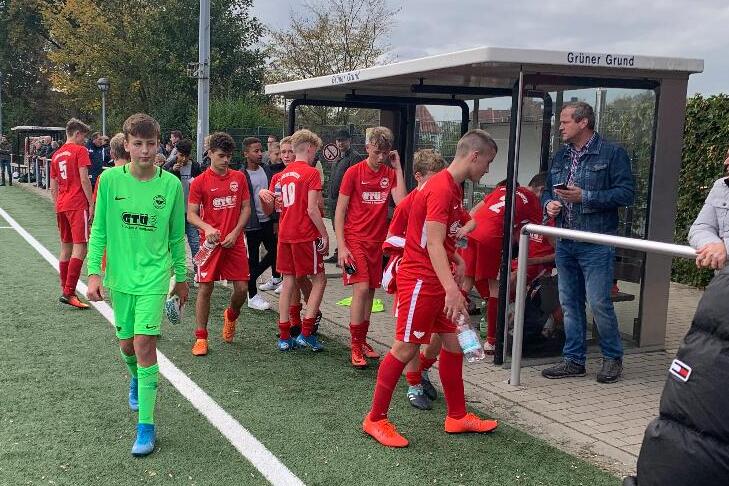 Gruppe junger Fu&szlig;ballspieler in roten Trikots verl&auml;sst das Spielfeld, w&auml;hrend ein Torwart in Gr&uuml;n zum Platz geht.