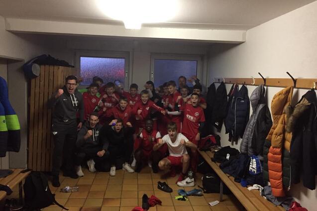 Gruppe junger Fu&szlig;ballspieler in einem Umkleidezimmer, posierend in Trikots vor B&auml;nken und Kleiderhaken.