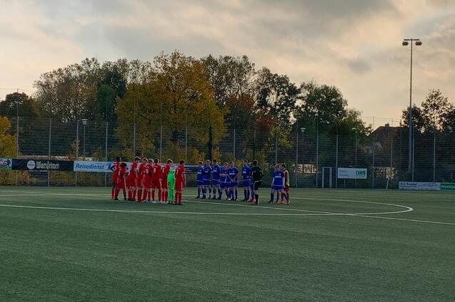Zwei Fu&szlig;ballmannschaften in roten und blauen Trikots stehen auf einem Kunstrasenfeld zusammen, um sich zu besprechen.