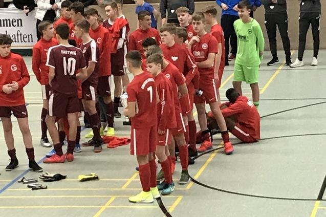 Gruppe von Jugendlichen in roten Fu&szlig;balltrikots versammelt auf einem Sportplatz, einige bereiten sich auf ein Spiel vor.