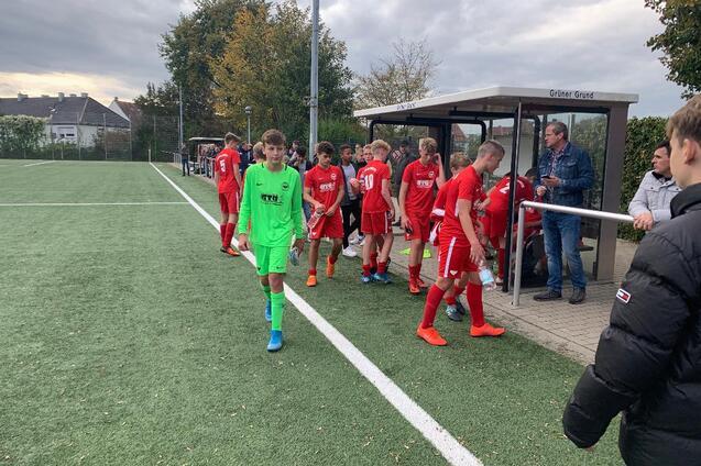 Gruppe junger Fu&szlig;ballspieler in roten Trikots verl&auml;sst das Spielfeld, w&auml;hrend ein Torwart in Gr&uuml;n zum Platz geht.