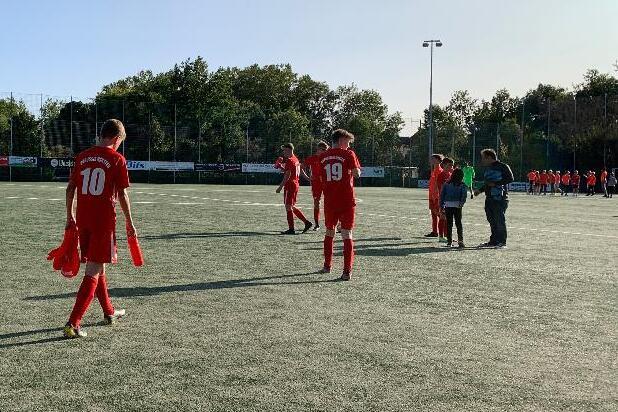 Spieler in roten Trikots verlassen den Fu&szlig;ballplatz, umgeben von B&auml;umen und einem klaren blauen Himmel.