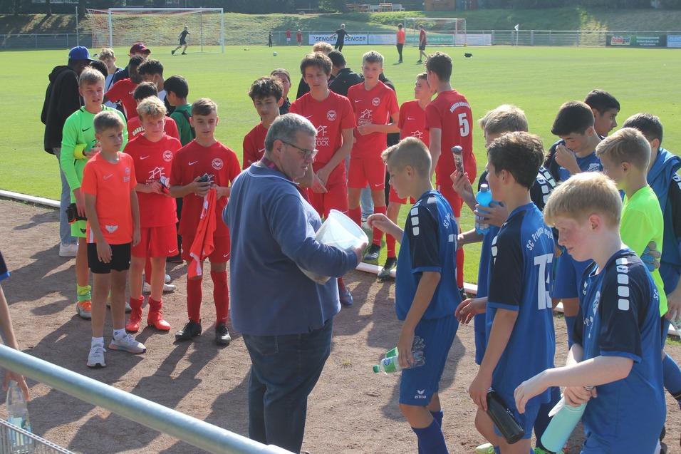 Gruppe von jungen Fu&szlig;ballspielern in verschiedenen Trikots versammelt sich um einen Trainer auf dem Sportplatz.