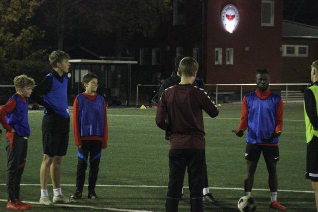 Gruppentraining von sieben Fu&szlig;ballspielern in blauen und roten Wams auf einem Kunstrasenplatz bei schwachem Licht.