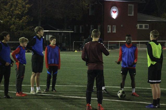 Gruppentraining von sieben Fu&szlig;ballspielern in blauen und roten Wams auf einem Kunstrasenplatz bei schwachem Licht.