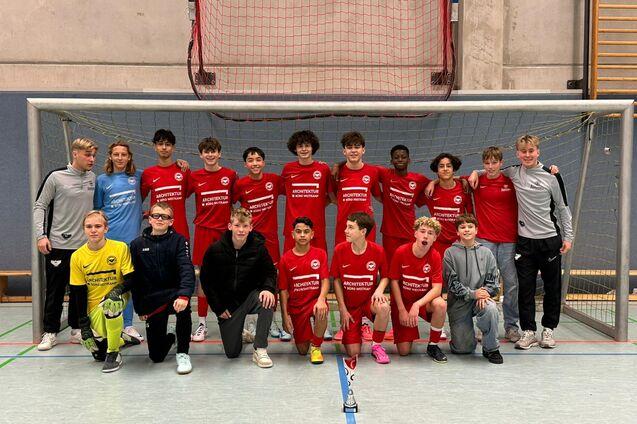 Gruppenfoto einer Fu&szlig;ballmannschaft in roten Trikots vor einem Tor in einer Sporthalle.