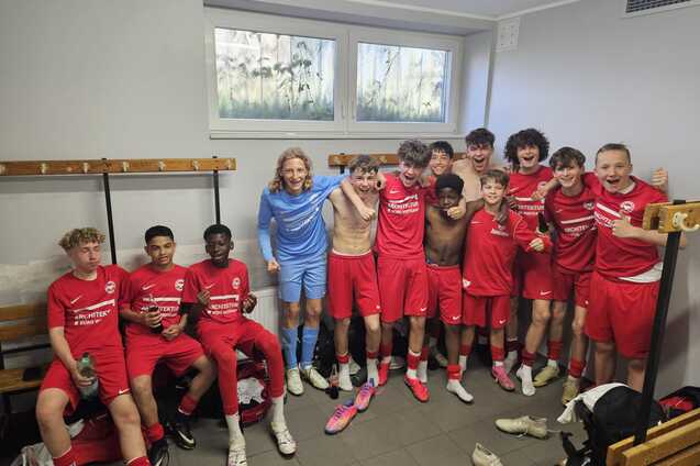 Gruppe von jungen Fu&szlig;ballspielern in roten Trikots l&auml;chelt freudig in der Umkleidekabine nach dem Spiel.