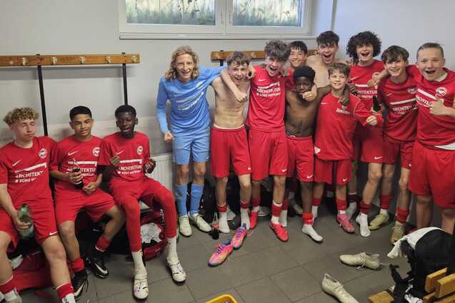 Gruppe von jungen Fu&szlig;ballspielern in roten Trikots l&auml;chelt freudig in der Umkleidekabine nach dem Spiel.