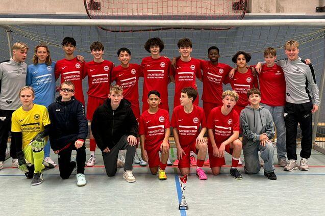 Gruppenfoto einer Fu&szlig;ballmannschaft in roten Trikots vor einem Tor in einer Sporthalle.