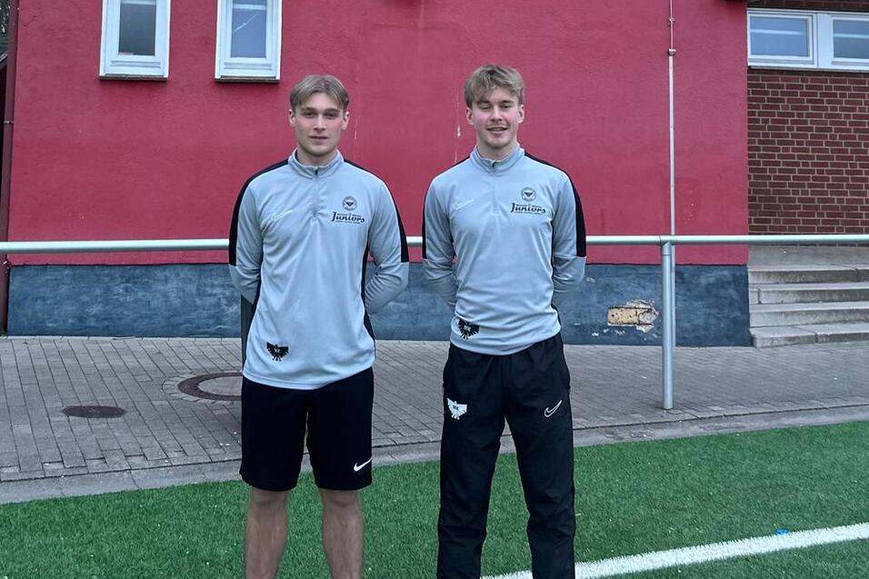 Zwei Jugendliche in Sportkleidung stehen vor einem roten Vereinsgeb&auml;ude mit dem Logo von Borussia M&uuml;nster.