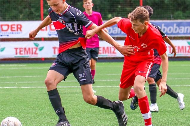 Zwei Jugendliche spielen Fu&szlig;ball auf einem Kunstrasenplatz, der Spieler in schwarz dribbelt den Ball, w&auml;hrend der in rot ihn versucht zu stoppen.