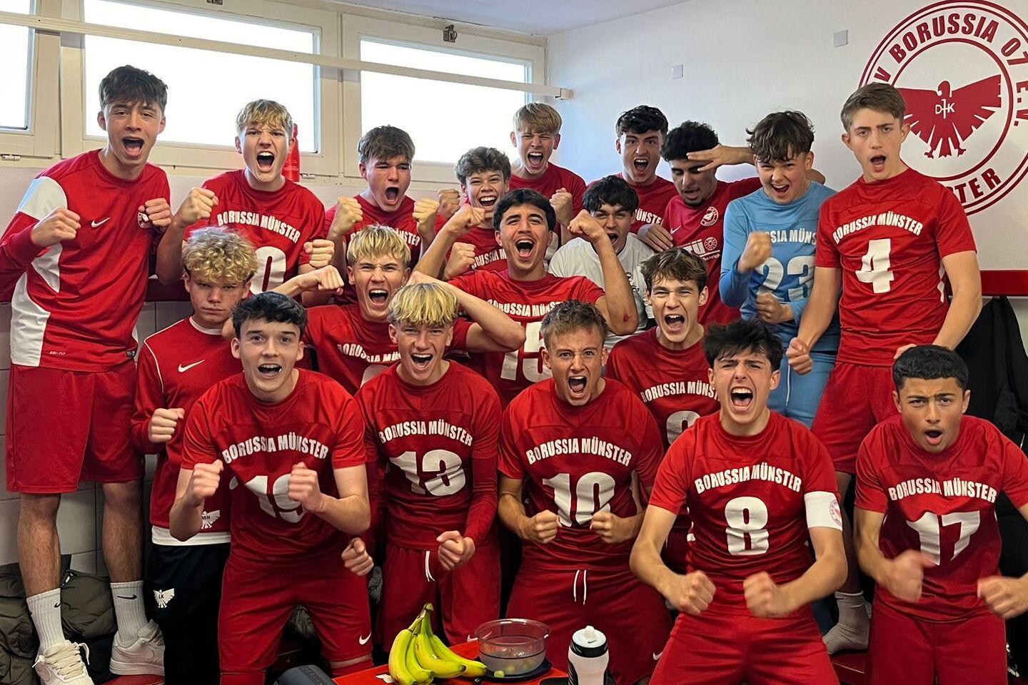 Gruppe junger Fu&szlig;ballspieler in roten Trikots jubeln fr&ouml;hlich in einem Umkleideraum.