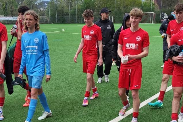 Gruppe junger Fu&szlig;ballspieler in roten Trikots verl&auml;sst das Spielfeld, begleitet von einem Trainer in schwarzer Kleidung.