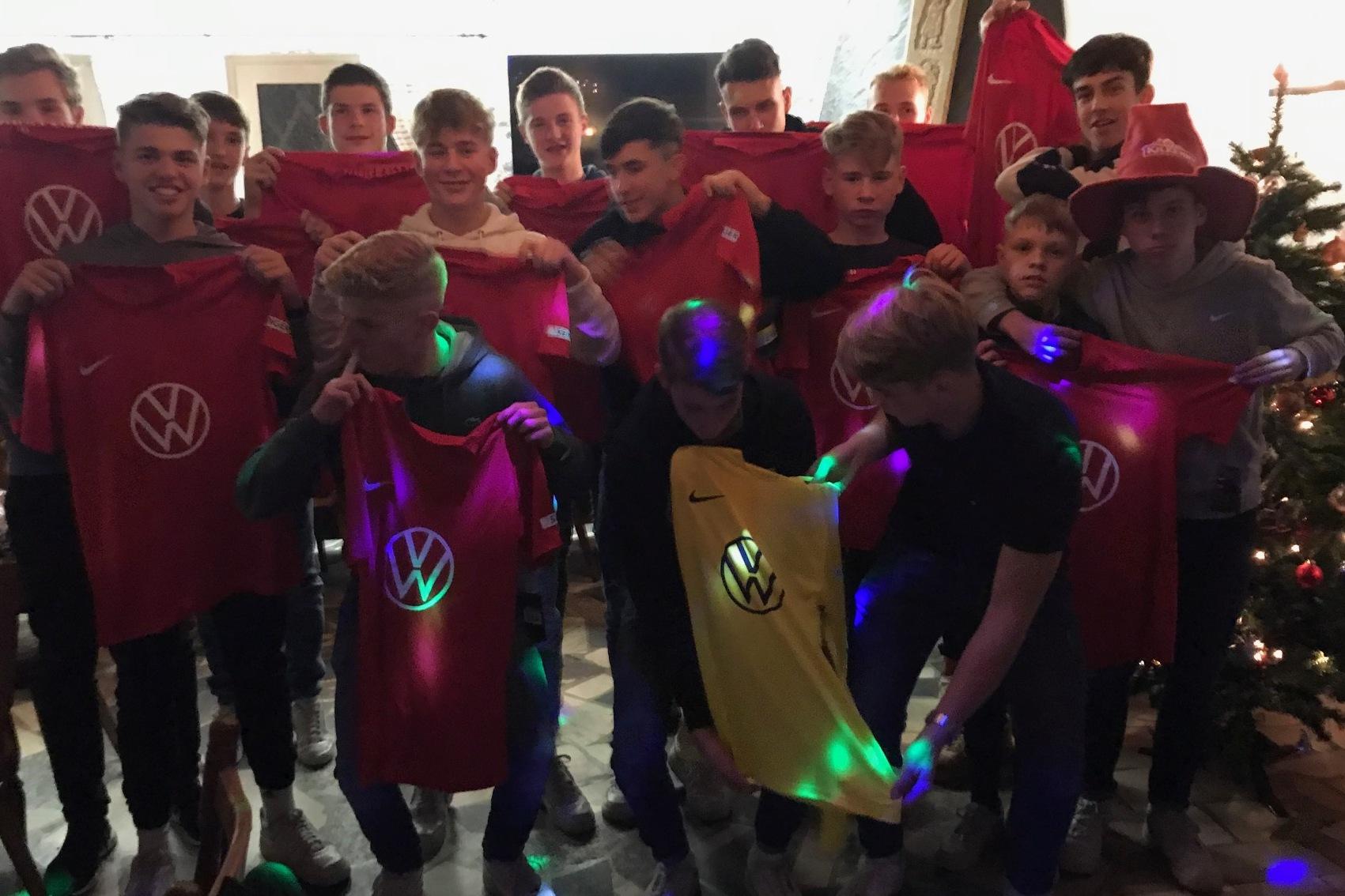 Gruppennahaufnahme von Jugendlichen, die rote und gelbe T-Shirts mit Volkswagen-Logo in einem festlich geschm&uuml;ckten Raum halten.