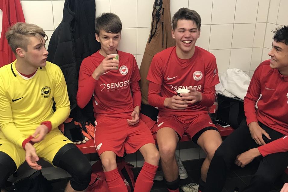 F&uuml;nf junge Fu&szlig;ballspieler in roter Sportkleidung sitzen in einer Umkleidekabine und unterhalten sich.
