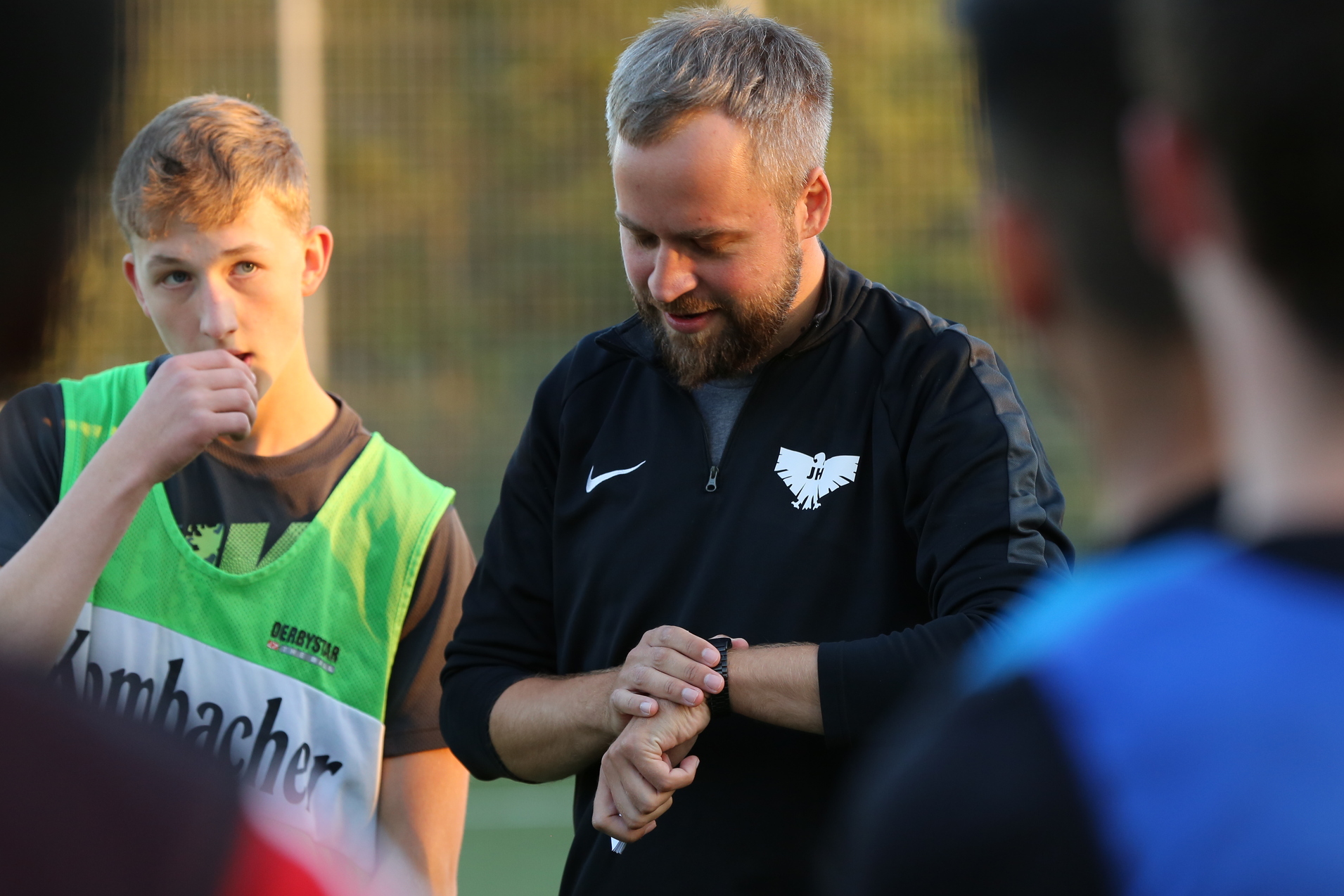 Trainer erkl&auml;rt Taktik an einer Sporteinheit, Spieler in gr&uuml;nem Trikot h&ouml;rt aufmerksam zu.