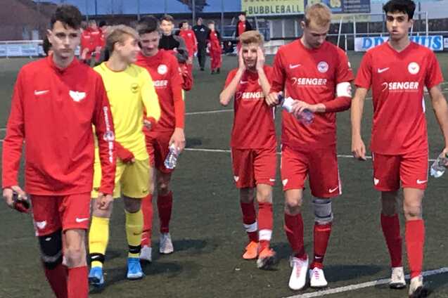 Gruppierung von Jugendlichen in roten Fu&szlig;balltrikots, die auf einem Kunstrasenplatz gehen, einige halten Wasserflaschen.