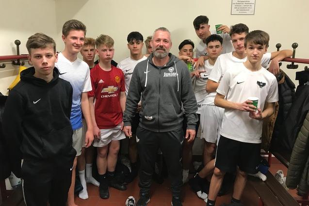 Gruppe von jungen Fu&szlig;ballspielern in einem Umkleideraum, umrahmt von einem Trainer in sportlicher Bekleidung.
