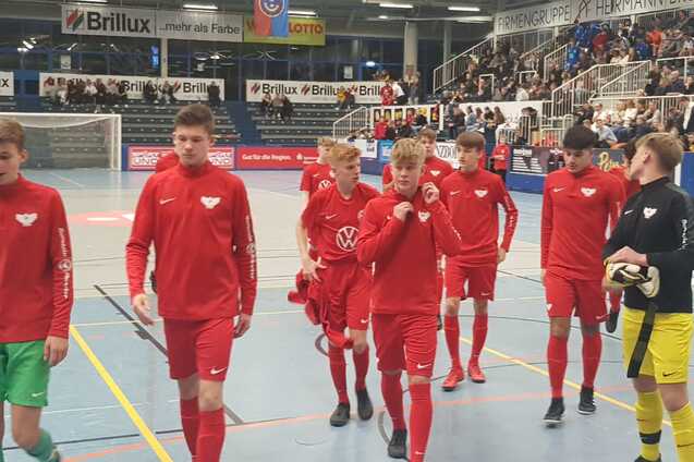 Gruppe von Jugendlichen in roten Sportanz&uuml;gen betritt eine Halle, im Hintergrund Zuschauer auf Trib&uuml;nen.