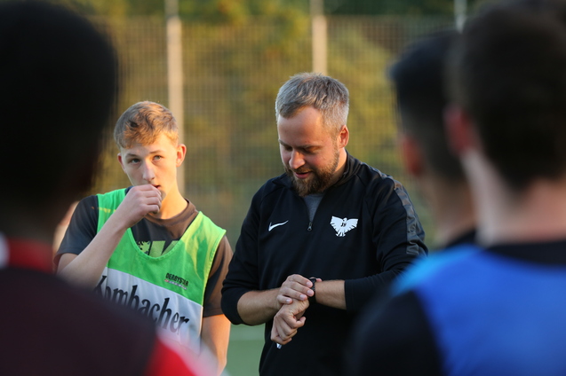 Trainer erkl&auml;rt Taktik an einer Sporteinheit, Spieler in gr&uuml;nem Trikot h&ouml;rt aufmerksam zu.