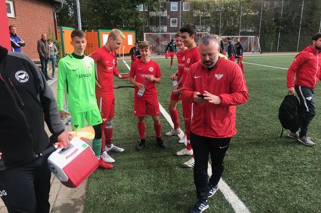 Gruppe von Jugendlichen in roten Fu&szlig;balltrikots auf dem Platz, Trainer bespricht sich mit ihnen.