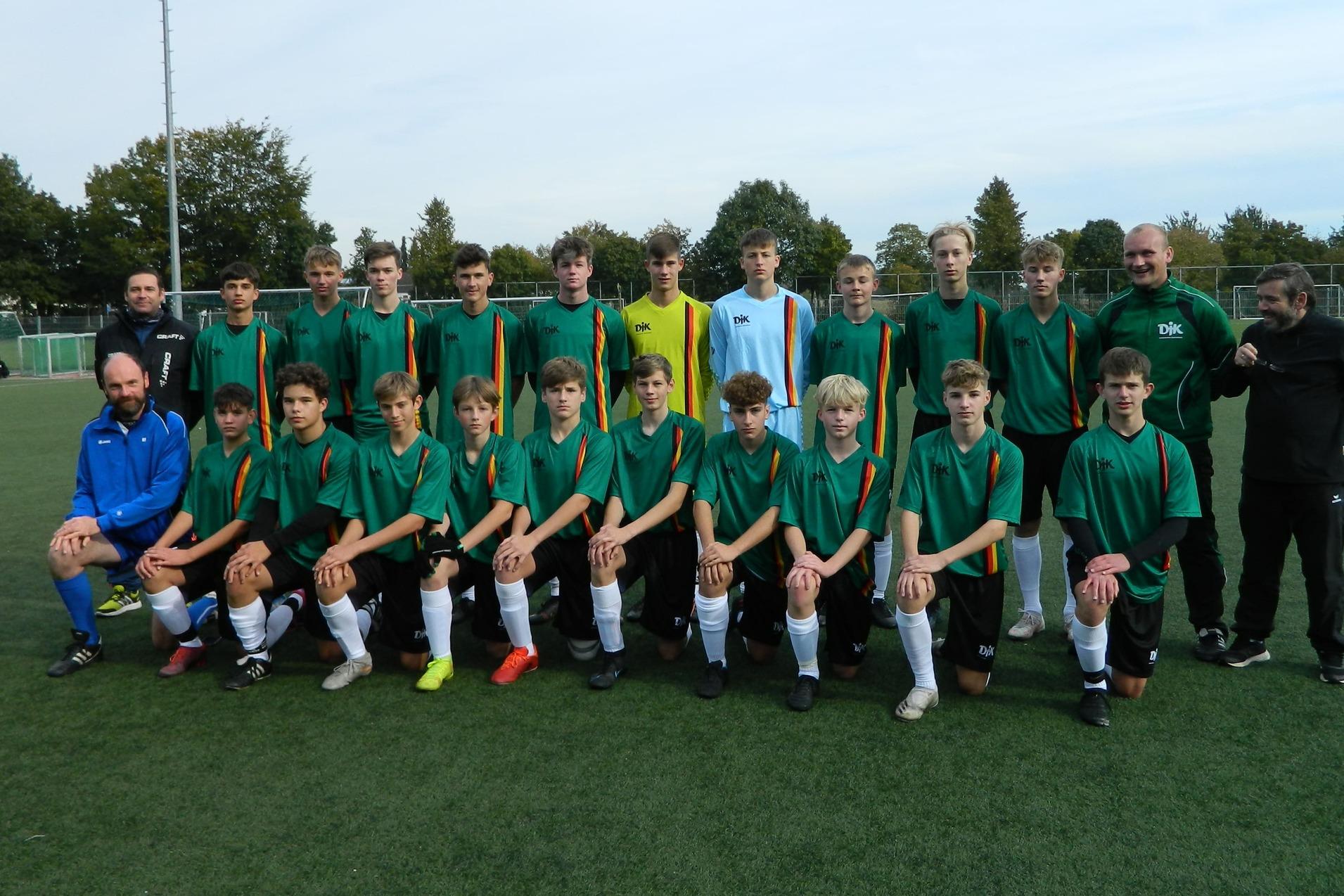Gruppenbild einer Fu&szlig;ballmannschaft mit 22 Spielern und Trainern, gekleidet in gr&uuml;ne Trikots, auf einem Rasenplatz.