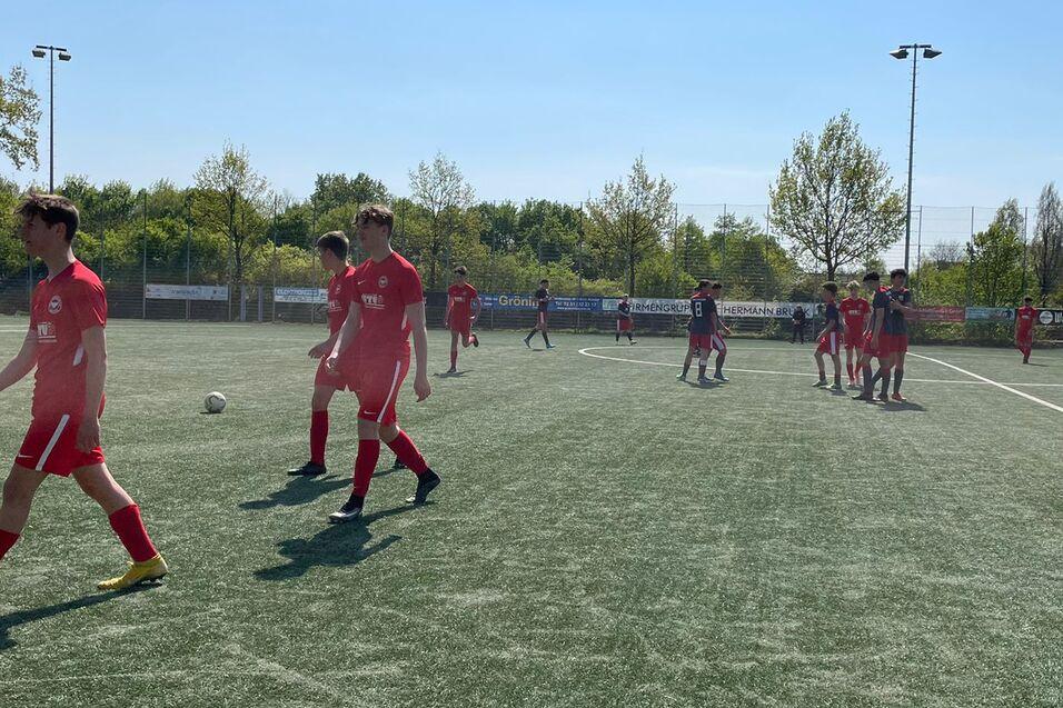 Fu&szlig;ballspiel mit Spielern in roten Trikots auf einem Kunstrasenplatz an einem sonnigen Tag.