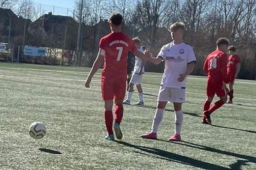 Zwei Jugendfu&szlig;ballmannschaften, eine in wei&szlig;en und eine in roten Trikots, spielen auf einem Kunstrasenplatz.