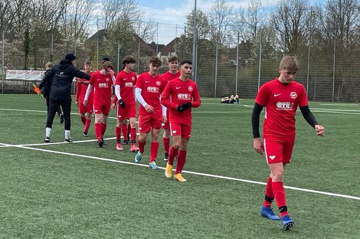 Gruppe von Jugendlichen in roten Fu&szlig;balltrikots geht auf einem Kunstrasenplatz in Richtung Spielfeldrand.