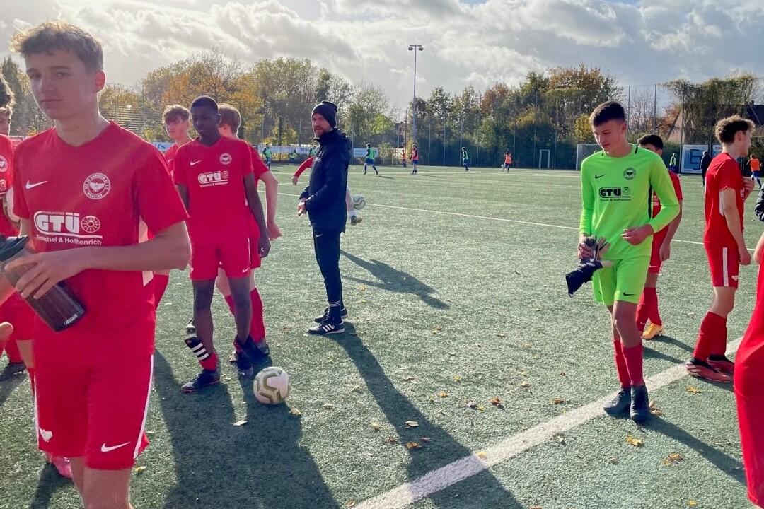 Junge Fu&szlig;ballspieler in roten Trikots stehen auf dem Platz, ein Torwart in Gr&uuml;n bereitet sich vor.