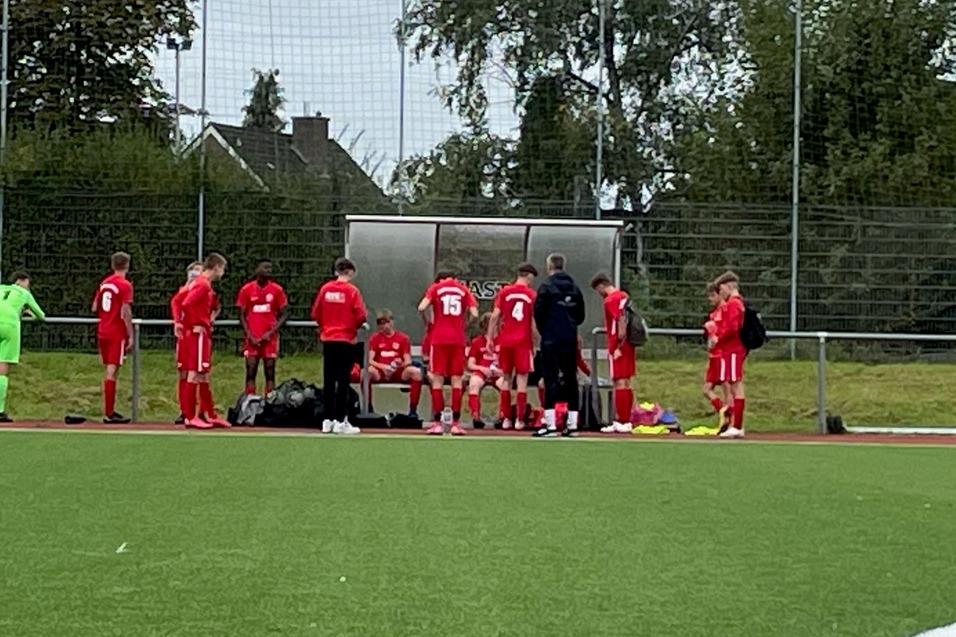Eine Gruppe von Fu&szlig;ballspielern in roten Trikots versammelt sich an einer Auswechselbank auf einem Sportplatz.