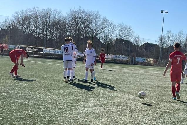Zwei Jugendfu&szlig;ballmannschaften, eine in wei&szlig;en und eine in roten Trikots, spielen auf einem Kunstrasenplatz.