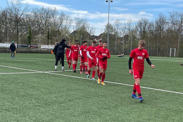 Gruppe von Jugendlichen in roten Fu&szlig;balltrikots geht auf einem Kunstrasenplatz in Richtung Spielfeldrand.