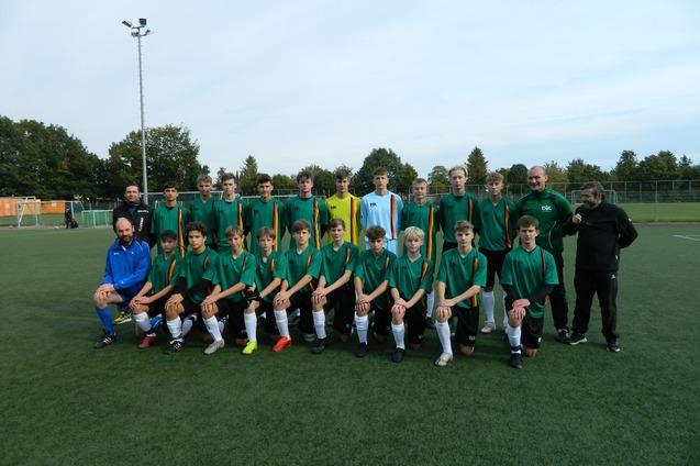 Gruppenbild einer Fu&szlig;ballmannschaft mit 22 Spielern und Trainern, gekleidet in gr&uuml;ne Trikots, auf einem Rasenplatz.