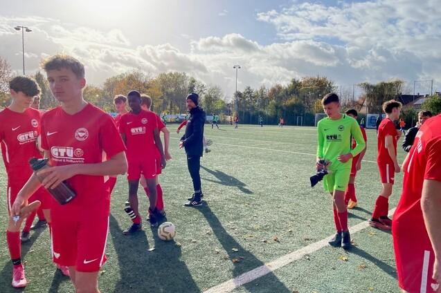 Junge Fu&szlig;ballspieler in roten Trikots stehen auf dem Platz, ein Torwart in Gr&uuml;n bereitet sich vor.