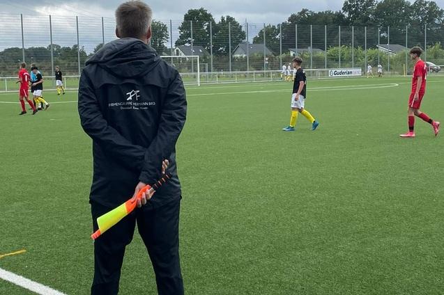 Ein Schiedsrichter mit Linienrichterflagge beobachtet ein Fu&szlig;ballspiel auf einem Kunstrasenplatz.