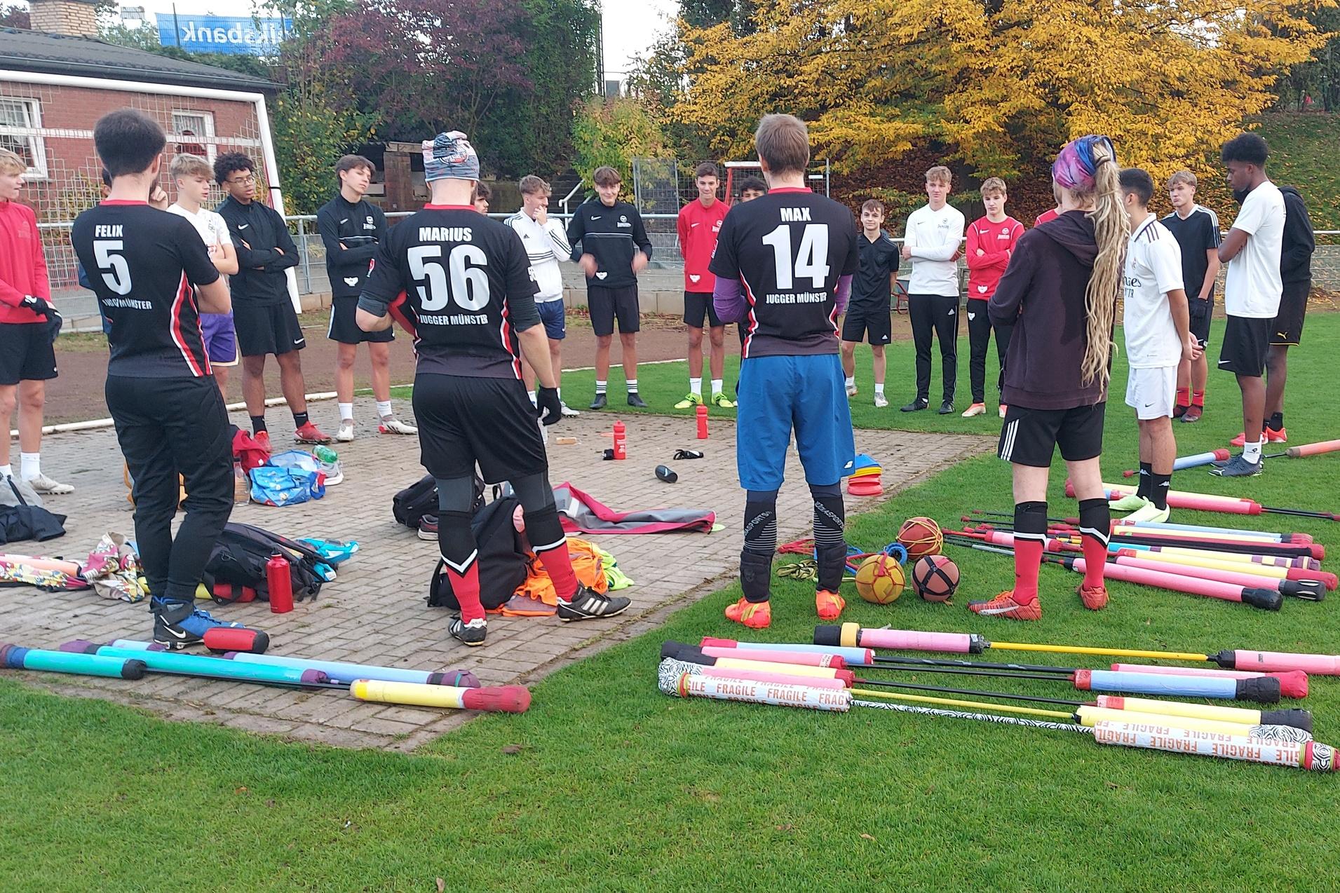 Gruppierung von Spielern in Sportkleidung auf einem Fu&szlig;ballplatz, umgeben von Trainingsmaterialien und Equipment.