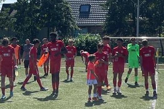 Gruppe von Fu&szlig;ballspielern in roten Trikots auf einem Rasenplatz, einige halten B&auml;lle und Pfeifen.