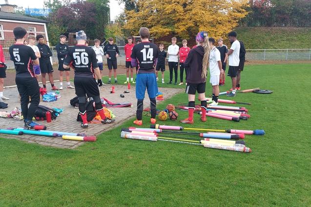 Gruppierung von Spielern in Sportkleidung auf einem Fu&szlig;ballplatz, umgeben von Trainingsmaterialien und Equipment.