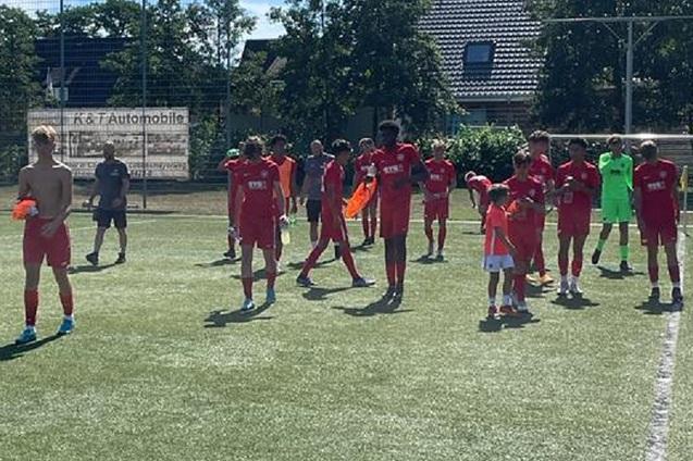 Gruppe von Fu&szlig;ballspielern in roten Trikots auf einem Rasenplatz, einige halten B&auml;lle und Pfeifen.