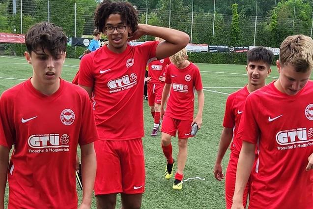 Gruppe von f&uuml;nf Jugendlichen in roten Sporttrikots, die auf einem Fu&szlig;ballfeld gehen.
