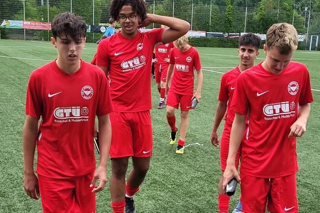Gruppe von f&uuml;nf Jugendlichen in roten Sporttrikots, die auf einem Fu&szlig;ballfeld gehen.