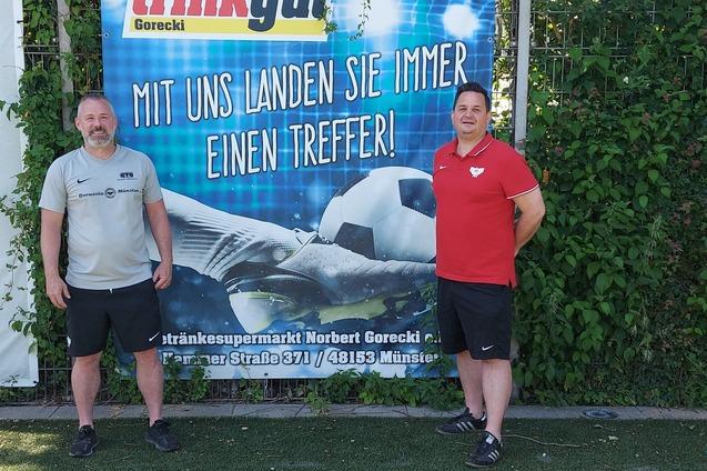 Zwei M&auml;nner stehen vor einem Werbebanner mit Fu&szlig;ball-Motiv und dem Text &bdquo;Mit uns landen Sie immer einen Treffer!&ldquo;
