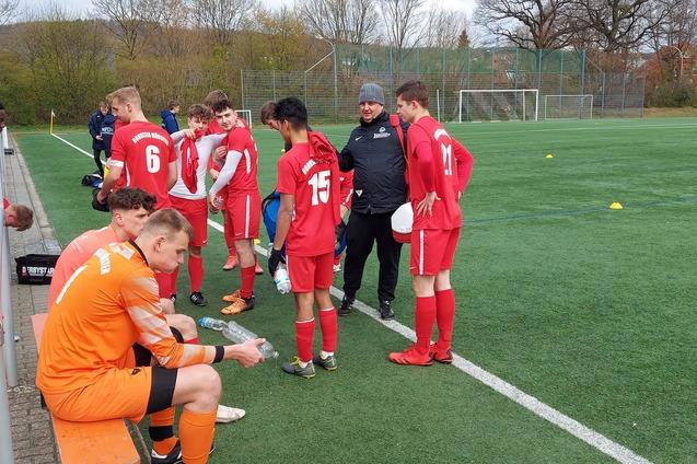 Fu&szlig;ballmannschaft in roten Trikots versammelt sich am Spielfeldrand. Ein Trainer spricht mit den Spielern.