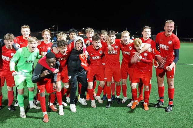 Gruppe jubelnder junger Fu&szlig;ballspieler in roten Trikots auf einem Kunstrasenplatz bei Nacht.
