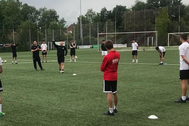 Gruppentraining auf einem Fu&szlig;ballplatz, Trainer steht vor einer Versammlung von Spielern in unterschiedlichen Trikots.