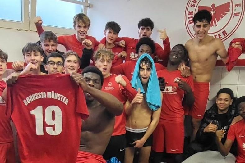 Gruppe von jubelnden jungen Fu&szlig;ballspielern in roten Trikots, einige halten ein Trikot mit der Nummer 19.