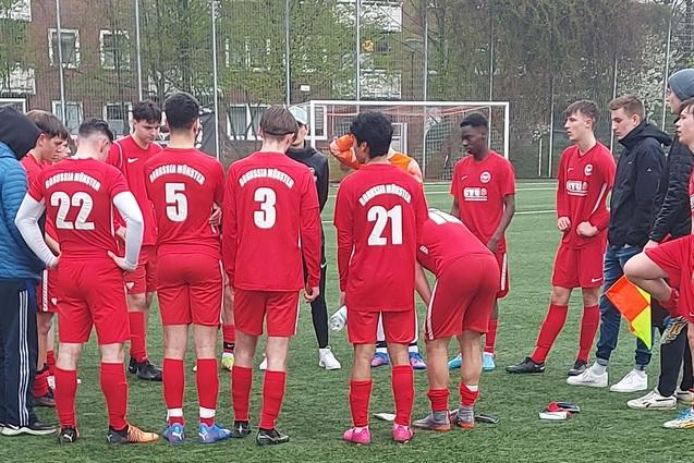 Gruppe junger Fu&szlig;ballspieler in roten Trikots versammelt sich auf dem Platz f&uuml;r eine Besprechung.